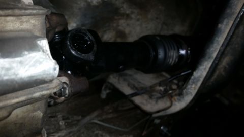 1985 Ford Bronco - A close-up view of a driveshaft and U-joint assembly connected to a vehicle's transmission or transfer case. The components are black and a…