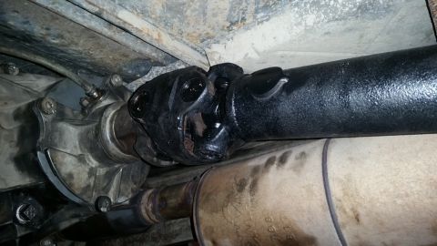 1985 Ford Bronco - A close-up view of the underside of a vehicle, showing the transfer case output shaft and the front of a driveshaft with a universal joint.…