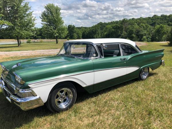 Green and white classic sedan with chrome trim and custom wheels parked on grass.