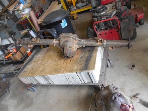 1992 Ford Bronco - A rusty Ford Bronco rear axle assembly is mounted on a wooden surface supported by concrete blocks. The scene takes place in a cluttered ga…