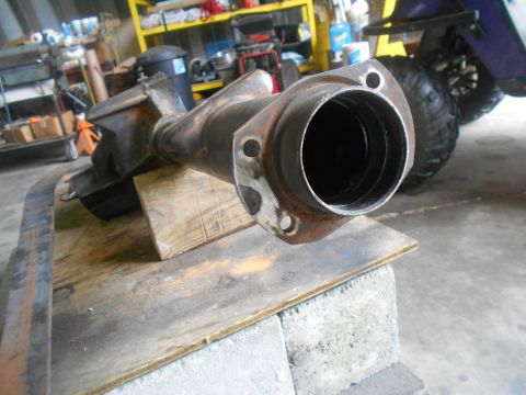 1992 Ford Bronco - A rusty differential housing is mounted on wooden blocks on a workbench. The housing is made of cast iron and has a flange with bolt holes…
