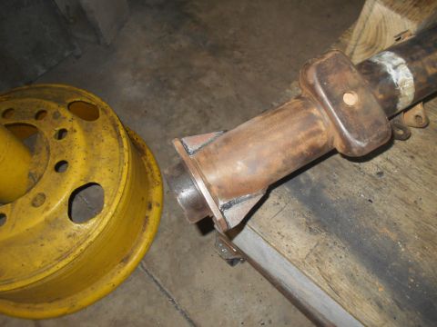 1992 Ford Bronco - A rusty metal axle assembly with a yellow wheel hub is shown in a workshop setting. The axle has a rectangular bracket welded to it, and a…