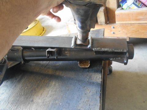 1992 Ford Bronco - A close-up view of a metal component, possibly part of a vehicle's suspension or frame, being held by a hand and resting on a workbench. Th…
