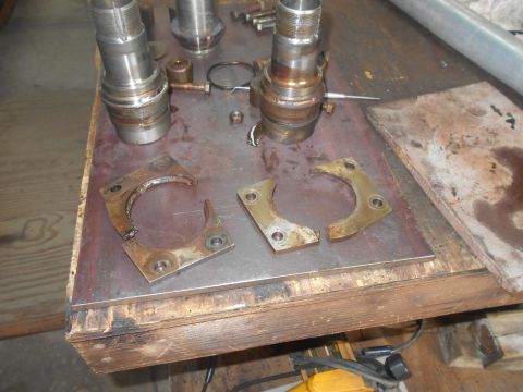 1992 Ford Bronco - Several metal parts, including two broken C-shaped brackets and two cylindrical metal components, are laid out on a wooden workbench. The s…