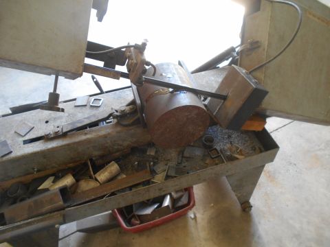 1992 Ford Bronco - A metal cutting saw is shown with a large round metal bar being cut. Metal shavings and cut pieces of metal are scattered around the saw.