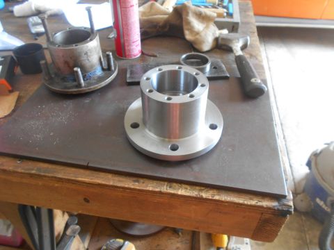 1992 Ford Bronco - Two metal wheel hubs are on a workbench. One hub is older and appears to have been welded, while the other is new and shiny. Various tools…