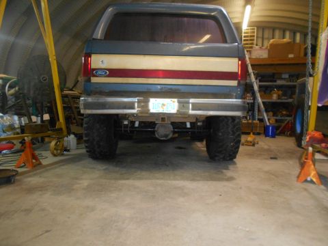 1992 Ford Bronco - The rear view of a lifted 1992 Ford Bronco is shown in a garage setting. The vehicle features large off-road tires and a red and white stri…