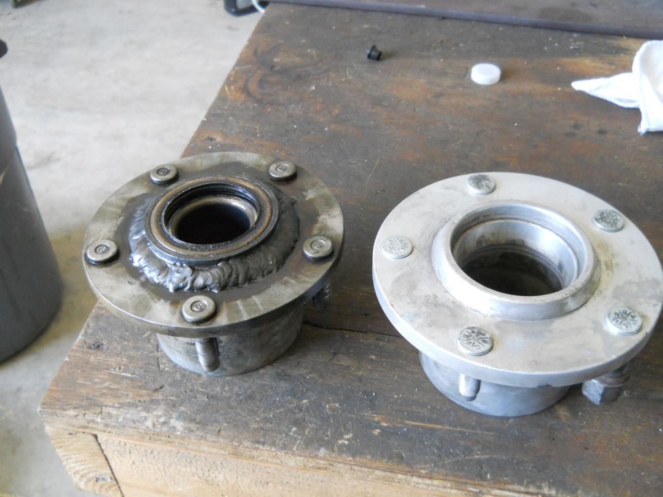 Two metal wheel hubs on a wooden workbench, one welded, one clean.