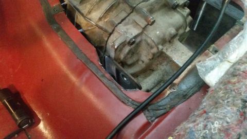 1985 Ford Bronco - A close-up view of a vehicle's transmission tunnel and part of the transmission housing. A metal bracket is bolted to the transmission and…