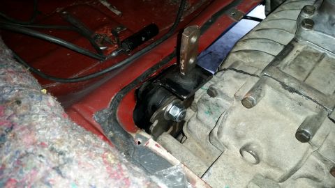 1985 Ford Bronco - A close-up view shows a black rubber and metal transmission mount bolted to the red floor pan of a vehicle, adjacent to the gray transmissi…