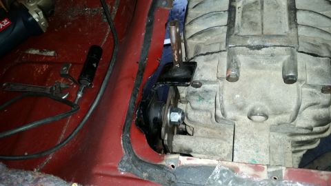 1985 Ford Bronco - Close-up view of a transmission mount bracket attached to a transmission housing. Tools, including an adjustable wrench and a flashlight, a…