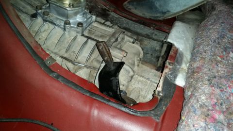 1985 Ford Bronco - A close-up view of a vehicle's transmission tunnel area, showing the shifter linkage and part of the transmission housing. Red interior tri…
