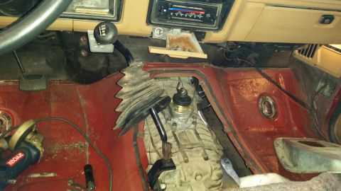1985 Ford Bronco - The interior of a vintage Ford Bronco shows the transmission tunnel with the transfer case and shifters exposed. An angle grinder is visibl…