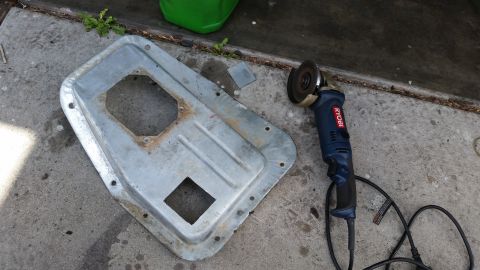 1985 Ford Bronco - A metal part with cutouts and an angle grinder are on a concrete surface.