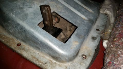 1985 Ford Bronco - A close-up view of a metal plate with a rectangular cutout, through which a dark-colored shift lever is visible. The plate is bolted to a v…