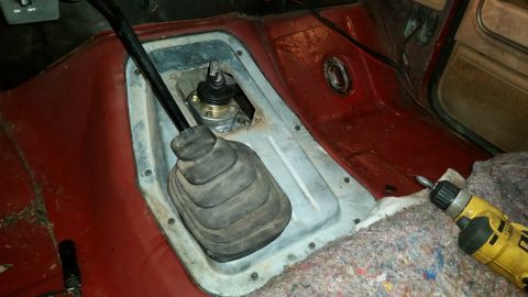 1985 Ford Bronco - Close-up of a manual transmission shifter assembly inside a vehicle, with a drill nearby.