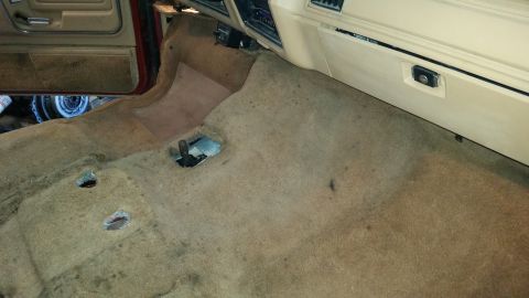 1985 Ford Bronco - The interior floor and dashboard of a vehicle are visible, with the carpet removed, revealing the underlying structure.