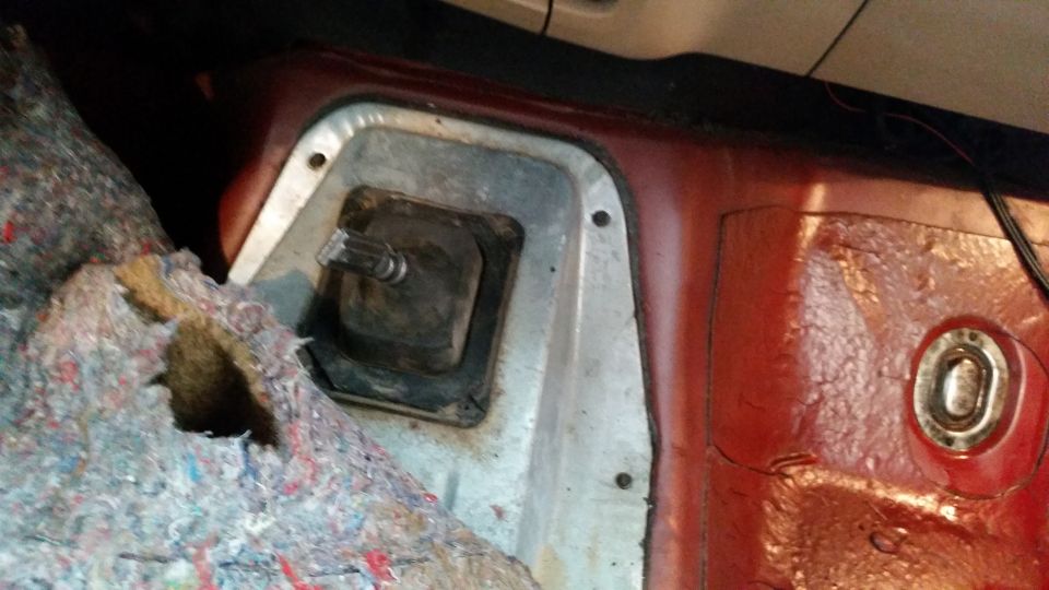 Close-up of a vehicle's transmission tunnel with carpeting removed, showing the shifter boot and surrounding metal