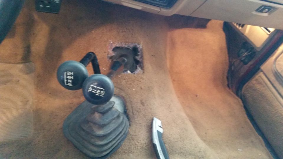 Interior view of a 1985 Ford Bronco showing the center console with two gear shifters and a cut-out for the transmission tunnel