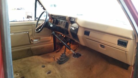 1985 Ford Bronco - The interior of a red truck is shown, a tan dashboard and door panels.