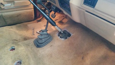 1985 Ford Bronco - The interior of a vehicle shows a removed floor section, exposing the transmission tunnel and shifter components.