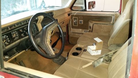 1985 Ford Bronco - The interior of a truck shows the dashboard, steering wheel, and tan seats with a center console.