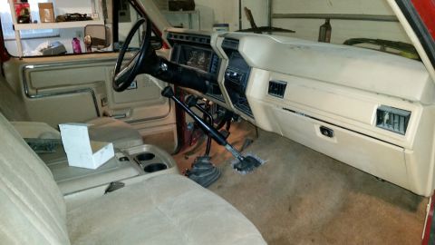 1985 Ford Bronco - The interior of a vintage Ford truck or SUV, a tan dashboard and dual shifters.