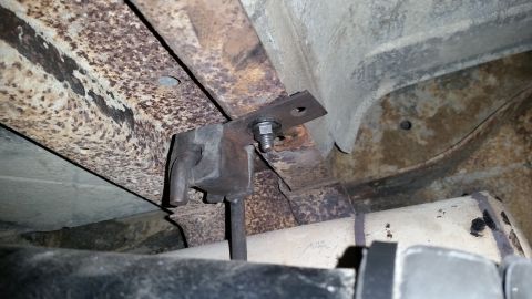 1985 Ford Bronco - Close-up view of the heavily rusted undercarriage of a vehicle, focusing on a mounting bracket and exhaust system components.