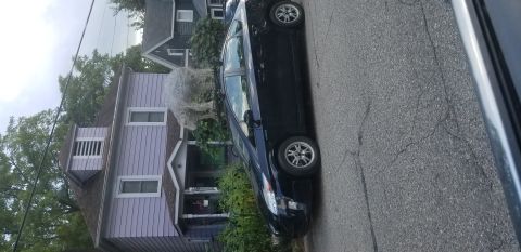 1995 Ford Bronco - A dark blue sedan is parked on the side of a street in front of a house.