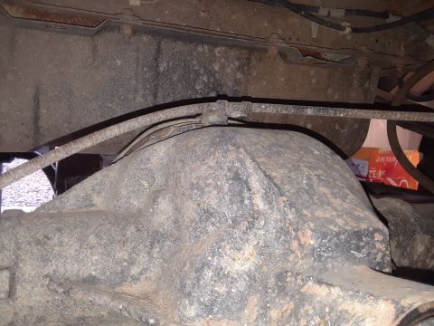 1985 Ford Bronco - Close-up view of a vehicle's rear axle assembly, showing brake lines and a portion of the tire. Text on a box in the background is partiall…