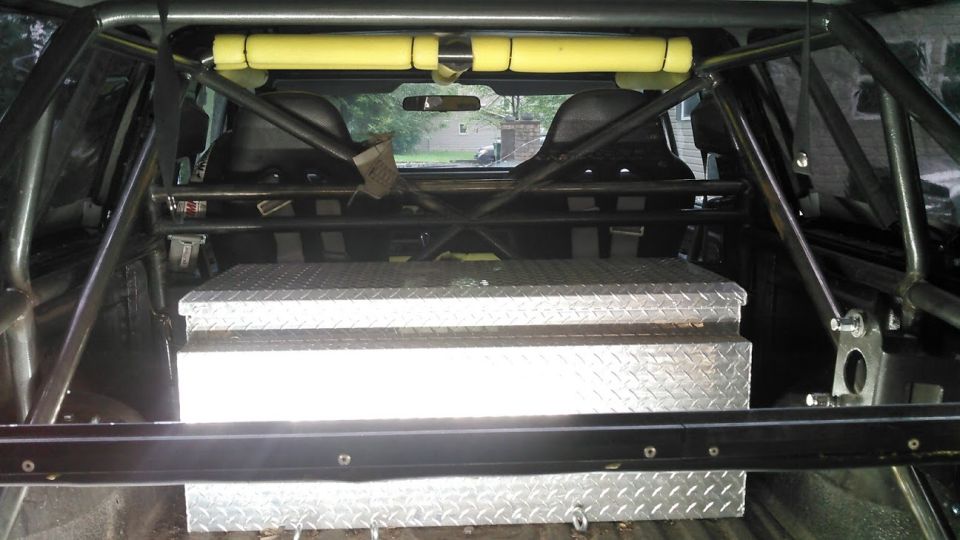 Vehicle interior showing roll cage, racing seats, and diamond plate toolbox