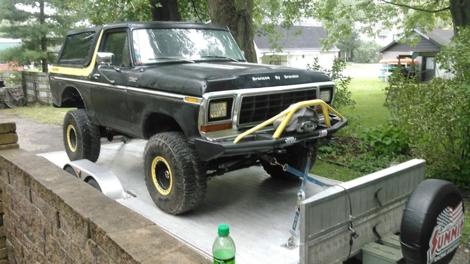 Black 1978 Ford Bronco with yellow trim, lifted on a trailer, with a yellow bull bar