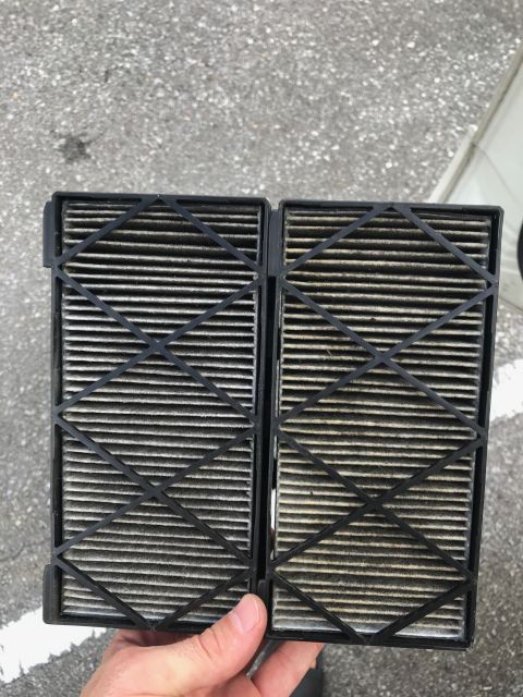 2002 Nissan Quest - A hand holds a dirty cabin air filter, showing its pleated filter media and black plastic frame.