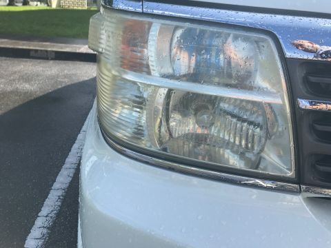 2002 Nissan Quest - Close-up of a white minivan's front headlight and grille, showing water droplets on the lens and chrome trim.