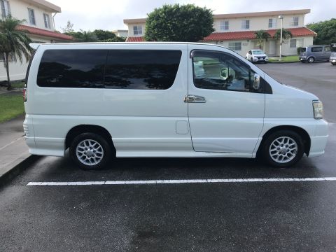 2002 Nissan Quest - Side view of a white minivan parked in a lot. Other vehicles and buildings are visible in the background.
