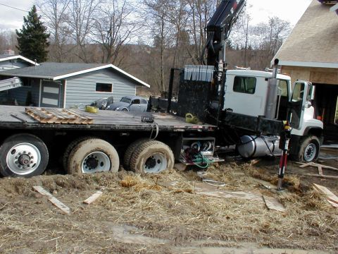 1983 Ford Bronco - A large crane truck is stuck in the mud, with its flatbed trailer partially submerged in the soft ground.