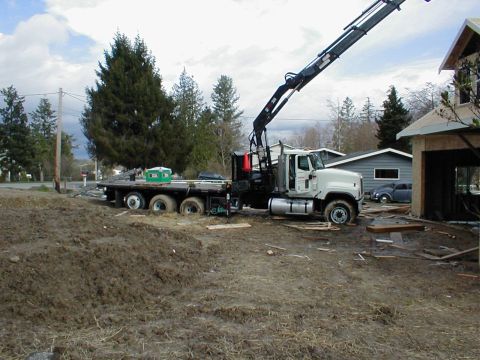 1983 Ford Bronco - A flatbed truck with a crane is parked on a muddy construction site near a house under construction.