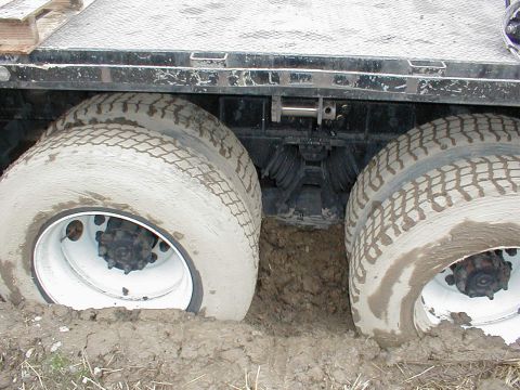 1983 Ford Bronco - The rear dual wheels of a truck are deeply embedded in mud, indicating it is stuck.