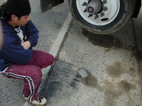 1983 Ford Bronco - A person crouches near a large truck tire, observing a dark puddle on the asphalt. The Supermotors.net logo is visible in the lower right c…