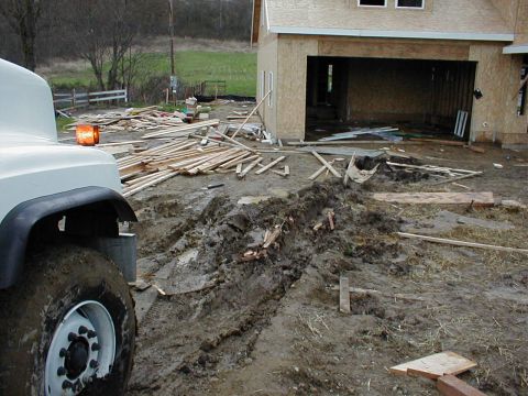 1983 Ford Bronco - Muddy tire tracks mark a construction site with lumber and an unfinished building.