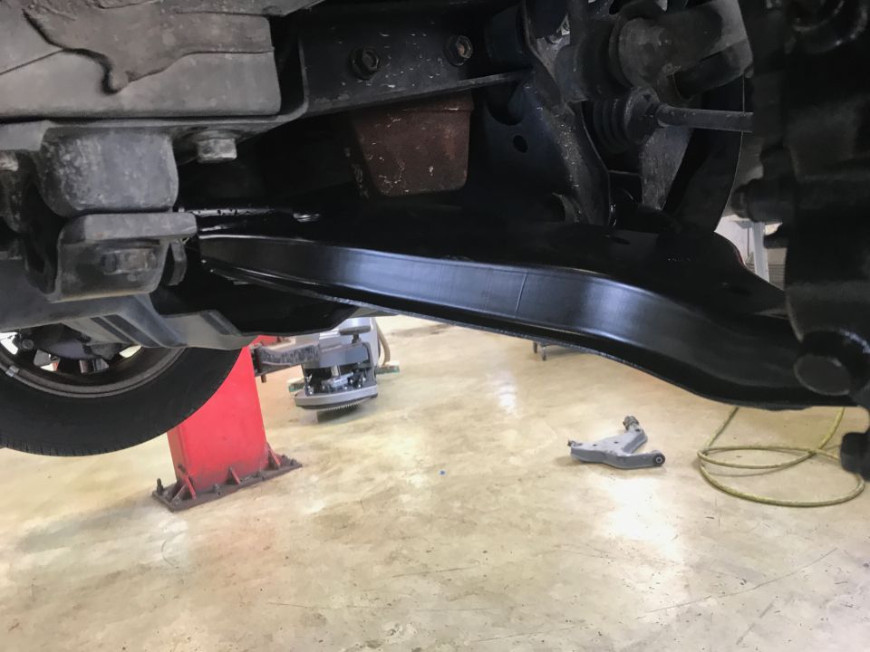 Underside of a vehicle's suspension with a black control arm, tire, and red lift.