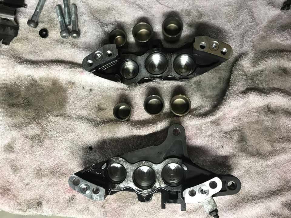 Disassembled motorcycle brake calipers with bolts and piston cups on a towel.