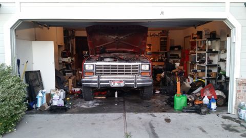 1985 Ford Bronco - A red 1985 Ford Bronco with its hood open is parked in a cluttered garage. The front of the vehicle is facing the camera, with various tool…