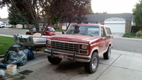 1985 Ford Bronco - A red 1980s Ford Bronco is parked in a driveway next to a boat on a trailer. The Bronco has a chrome grille and a license plate that reads…