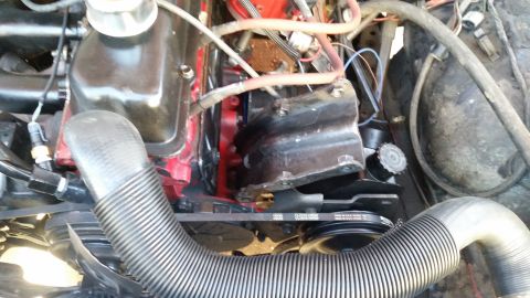 1985 Ford Bronco - A close-up view of a V8 engine bay, showing the red engine block, black valve covers, and various hoses and belts. A ribbed intake hose is…