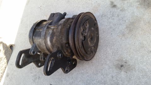 1985 Ford Bronco - A used automotive air conditioning compressor with a pulley is shown resting on a concrete surface. The compressor is black and silver and…