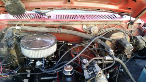 1985 Ford Bronco - The image shows a close-up view of the engine bay of a red Ford Bronco, focusing on the air filter assembly, carburetor, and various hoses…