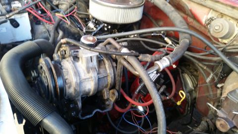 1985 Ford Bronco - The image shows a close-up view of a vehicle's engine bay, focusing on the air conditioning compressor and various hoses and wiring. The en…