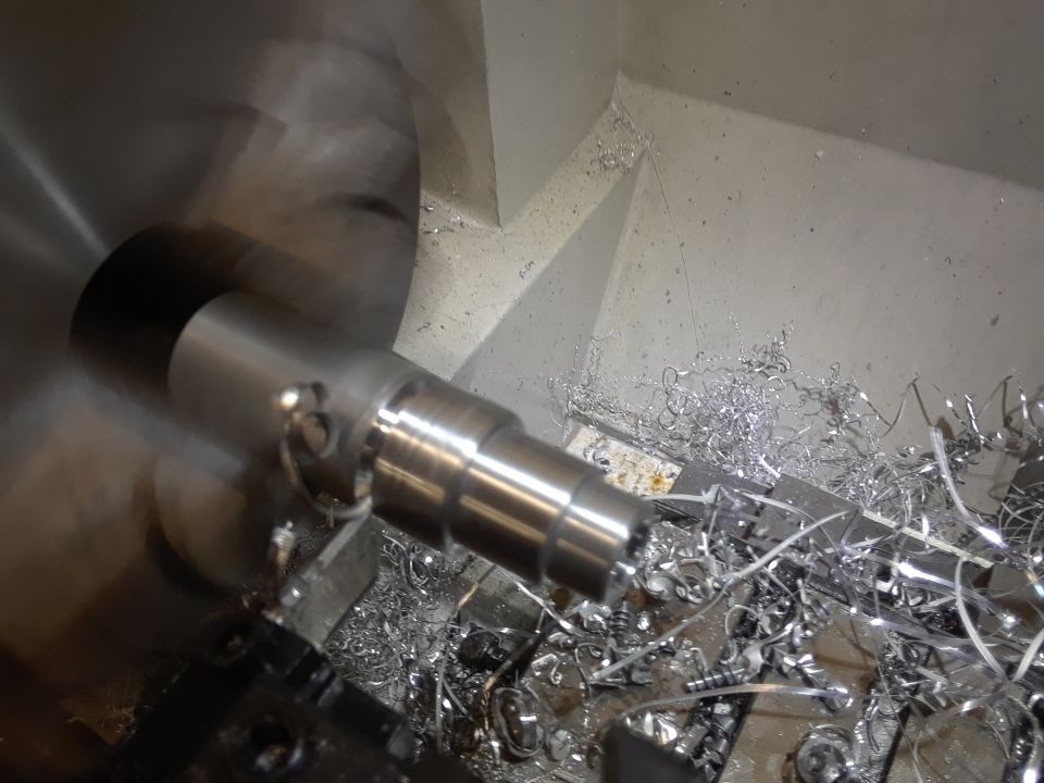 Metal workpiece being machined on a lathe with metal shavings.