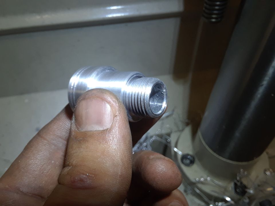 Close-up of a threaded metal part held by a person's thumb and forefinger.